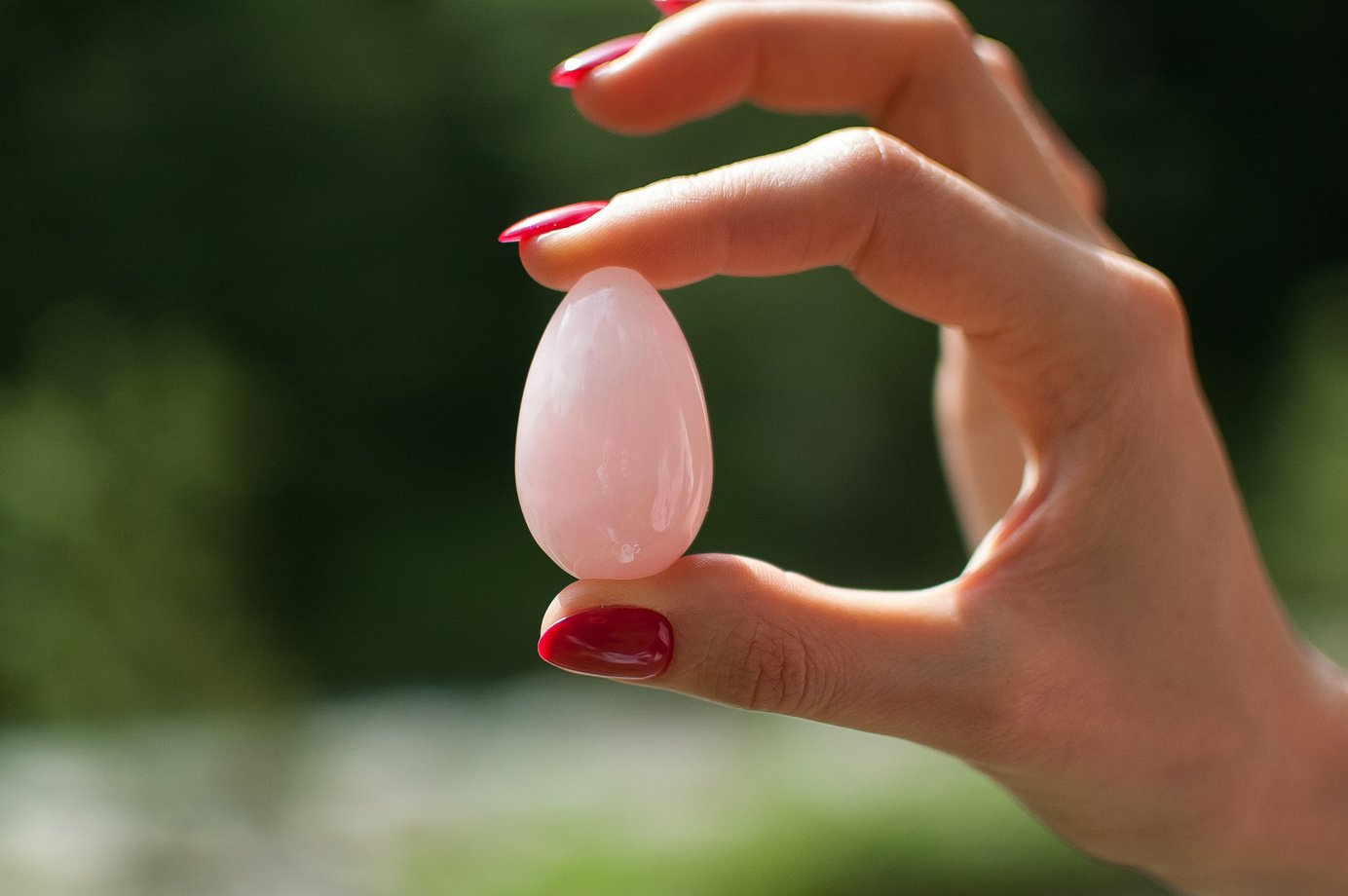 Close up photo of female hand holding a yoni egg. Rose quartz crystal egg on river background. Womens health concept